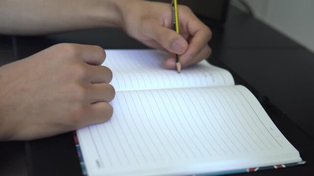 Close-up selective focus of a person writing in an open blank lined diary notebook with a pencil.