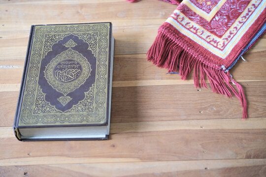 A Quran and a prayer mat on a wooden table, with empty space for text.