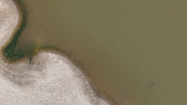 Aerial view of the Po riverbank showing exposed sandy shore and low water levels during a summer heatwave in Cremona, Lombardy, Italy.