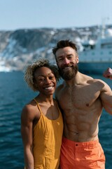 Fototapeta premium Smiling couple in coordinated yellow swimwear near icy water with a ship for travel poster and adventure background design
