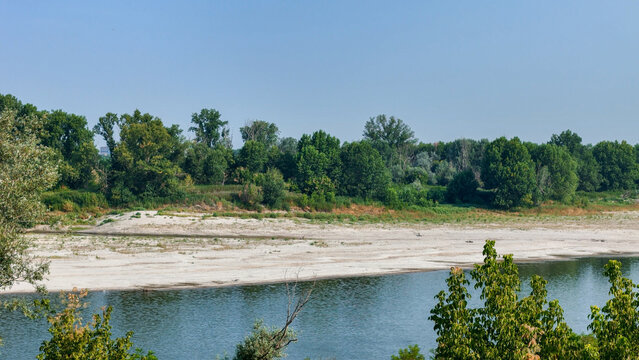 Aerial view of the Po River showing exposed sandbanks due to low water levels during a summer heatwave, surrounded by lush green trees in Cremona, Lombardy, Italy.