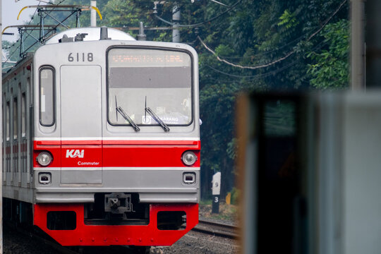 Jakarta, Indonesia - August 5, 2026: Close-up view of a KAI Commuter Tokyo Metro 6000 Series train, unit 6118, passing through a green, tree-lined railway corridor.