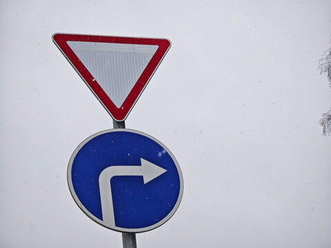 Signpost showing a yield sign and a right turn sign during snowfall