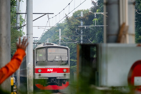 Jakarta, Indonesia - August 5, 2026: KAI Commuter JR 205 Series train approaches a level crossing as a railway officer in an orange jacket waves a hand signal.