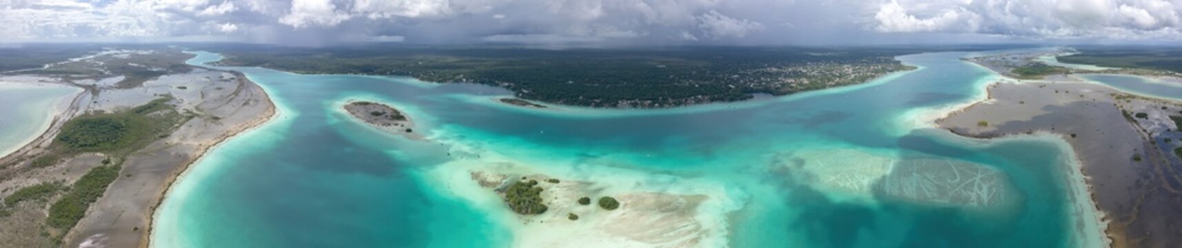 Aerial view of Bacalar Lagoon featuring turquoise waters, small islands, and lush vegetation under a cloudy sky in Bacalar, Quintana Roo, Mexico.