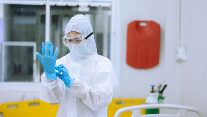 Healthcare Worker Adjusting Blue Rubber Gloves Wearing Full PPE Suit and Goggles for Infection...