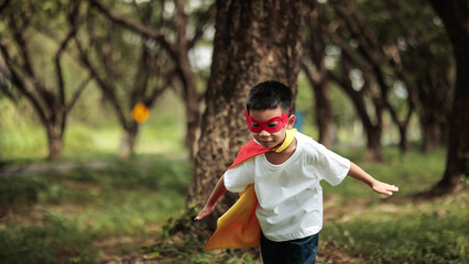 Cute Asian Boy in Superhero Costume Running with Arms Spread Flying Pose for Child Imagination Concept in Park © vittaya