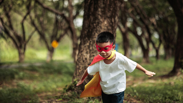 Cute Asian Boy in Superhero Costume Running with Arms Spread Flying Pose for Child Imagination Concept in Park
