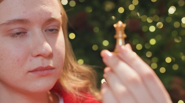 Focused caucasian woman studying golden queen piece in dim cafe, serious strategist evaluating move, intense stare, cinematic bokeh and brick backdrop, analytical mood and steady hands.