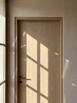 Minimalist wooden door with window shadow and rainbow light reflections on wall