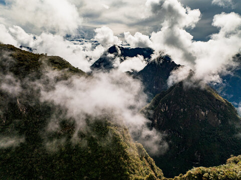 Aerial view of the Historic Sanctuary of Machu Picchu surrounded by lush green mountains and dramatic clouds in the Andes, Urubamba Province, Cusco, Peru.