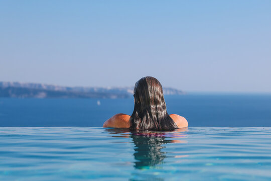 A woman relaxes in an infinity pool overlooking the Aegean Sea in Santorini, Greece, reflecting the calm beauty and luxurious simplicity of Mediterranean island life.