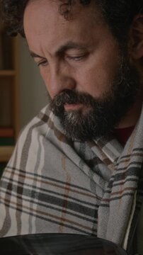 Vertical shot of middle aged Caucasian man wrapped in blanket holding and blowing dust off vinyl record. Clip is ideal for retro music, hobby, or nostalgia marketing campaigns