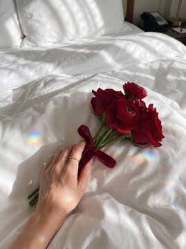 Hand holding red rose bouquet on white bed sheet with prism light reflection