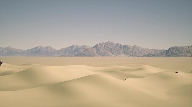 Golden sand dunes rise and fall gently under a brilliant blue sky, creating a tranquil scene in the heart of the desert, where mountains stand majestically in the background.
