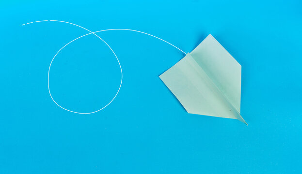 Green paper airplane following a looping white flight path on blue background
