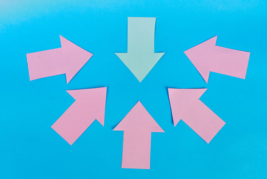 One green and five pink paper arrows pointing toward the center on blue background
