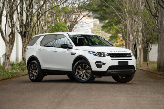 White Land Rover Discovery Sport front three quarters view outdoors, Luxury SUV on tree lined paved road