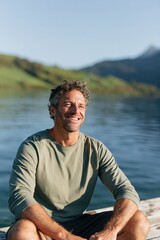 Fototapeta premium Man sitting on a dock by a calm lake smiling in golden sunlight for wellness banner and summer background