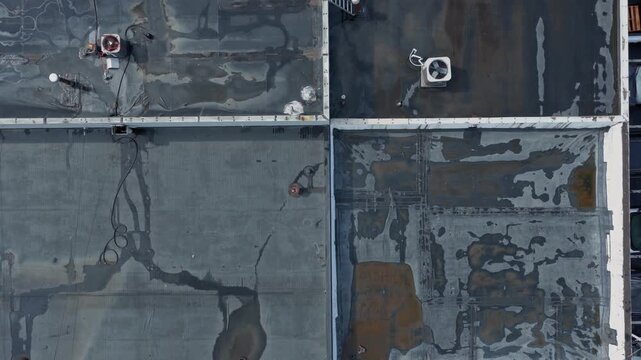Rain and water damage across industrial commercial business rooftop and flat roof on rubber sealed roofing causing leaks, rainfall tears, and leaking into building exterior from above drone aerial 4k