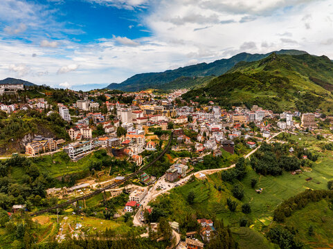 Aerial view of Sa Pa town nestled in the lush green mountains of the Hoang Lien Son range, featuring colorful buildings, winding roads, and terraced landscapes in Sa Pa, Lao Cai, Vietnam.