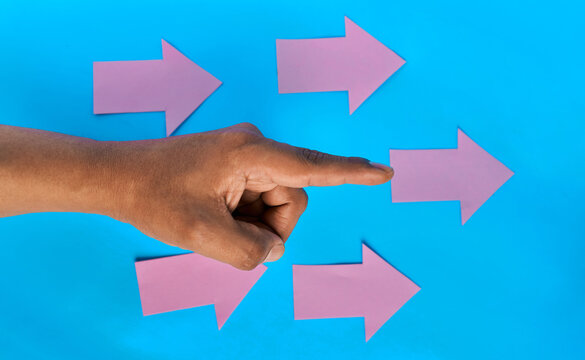 Hand pointing toward one of several pink right arrows on blue background
