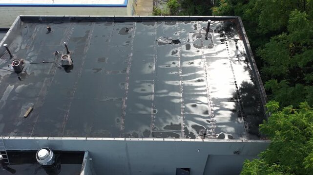 Rain and water damage across industrial commercial business rooftop and flat roof on rubber sealed roofing causing leaks, rainfall tears, and leaking into building exterior from above drone aerial 4k