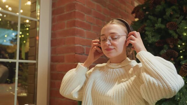 Woman reading book in cafe at window table with headphones and mug, chunky sweater and soft festive lights frame studious scene as she turns pages like student, editor, or booklover immersed