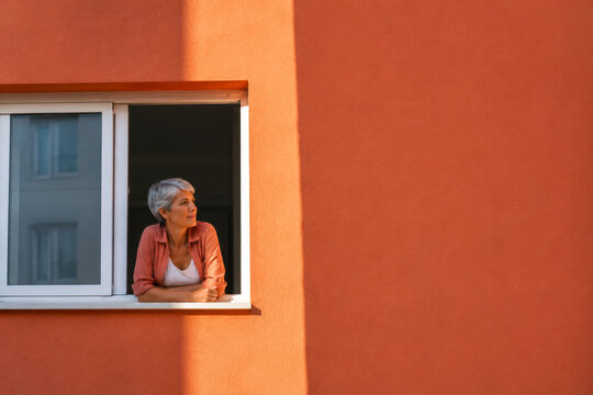 Mature Woman Taking a Quiet Break by an Open Window with Warm Sunlight and Copy Space
