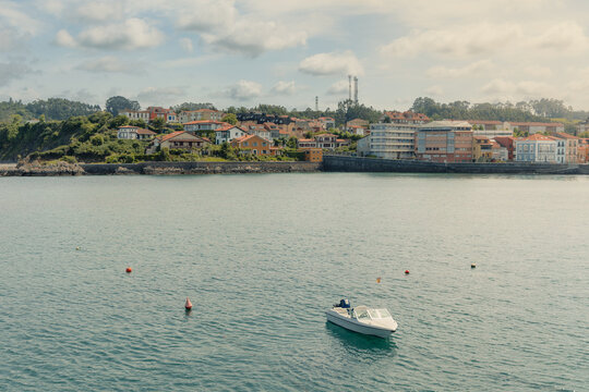 Coastal town of Luanco, Asturias, Spain, seeing houses and buildings along the harbor, a white motorboat floating on the calm sea water, reflecting the serene atmosphere