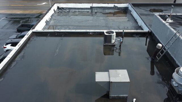 Rain and water damage across industrial commercial business rooftop and flat roof on rubber sealed roofing causing leaks, rainfall tears, and leaking into building exterior from above drone aerial 4k