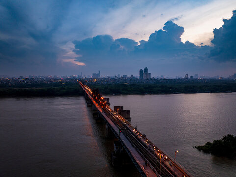 Aerial view of Long Bien Bridge spanning the Red River at twilight with city lights reflecting on the water in Hong Ha, Ha Noi, Vietnam.