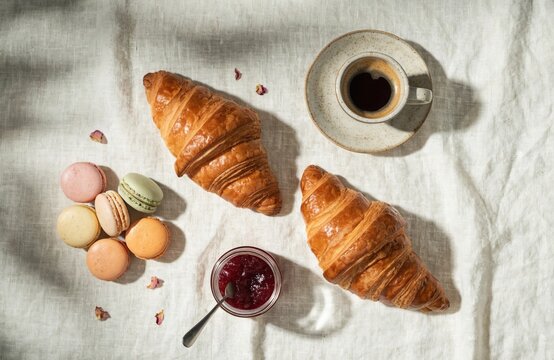 A delightful arrangement of french pastries showcasing flaky croissants vibrant macarons and a steaming cup of coffee set on a linen tablecloth for a charming breakfast atmosphere