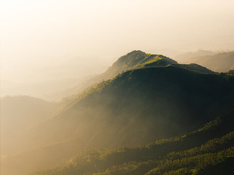 Aerial view of Dieng Plateau with lush green mountain ridges and slopes illuminated by warm golden hour light in Indonesia.
