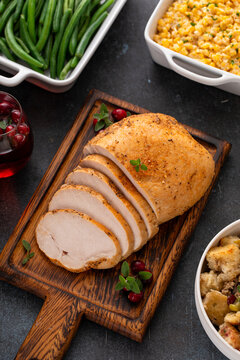 Roasted turkey breast sliced on a cutting board with all Thanksgiving sides