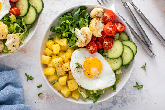 Healthy breakfast or lunch bowl with cooked potatoes, fresh vegetables and fried egg