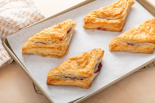 Puff pastries turnovers with cherry or berry jam on a baking sheet freshly baked and ready to eat