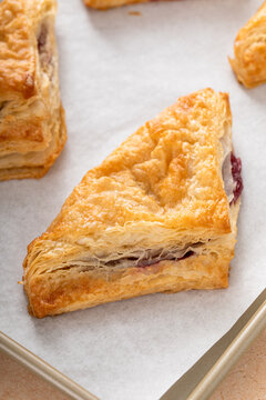 Puff pastries turnovers with cherry or berry jam on a baking sheet freshly baked and ready to eat