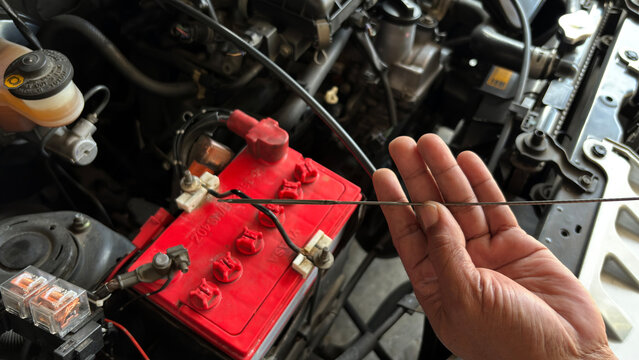 Close-up of car engine bay showing red battery with cables and hand holding dipstick to check fluid levels. Perfect for automotive diagnostics, repair, and maintenance concepts.