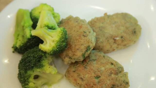 Homemade fish patties served with steamed broccoli on a white ceramic plate