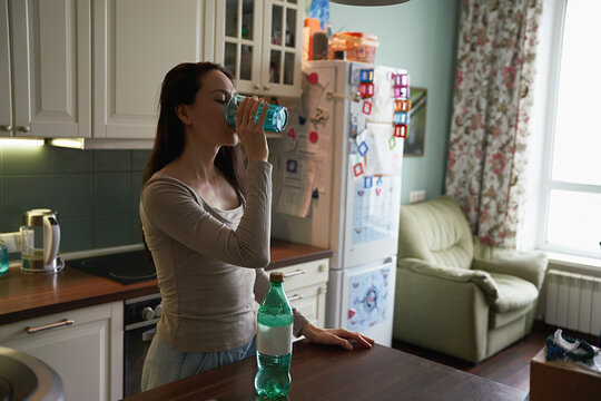 Woman drinks water in a kitchen at home in the afternoon
