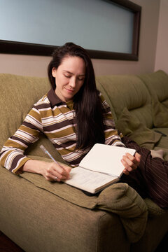 Woman writes in a notebook while sitting on a couch