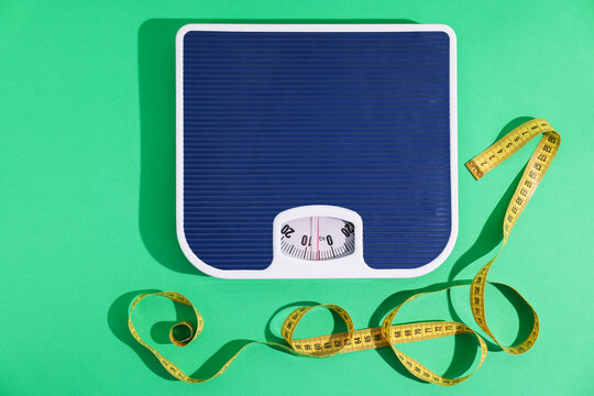 Scales with measuring tape on green background, flat lay