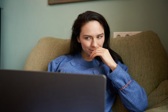 Woman sits on couch while using laptop at home
