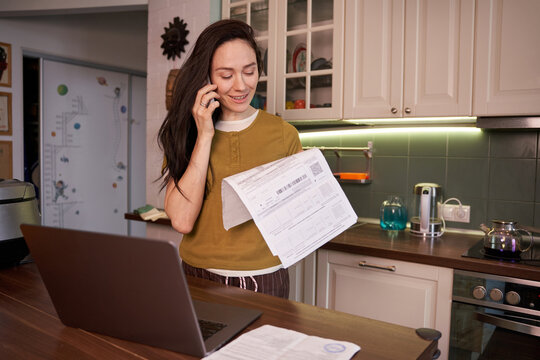 Woman talks on phone while holding documents in kitchen