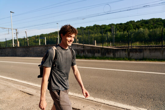 Young Man Walks Along a Road Near Green Fields During the Day