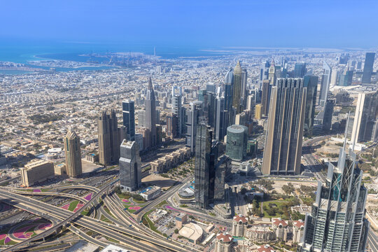 Aerial view of the modern skyline of Dubai featuring towering skyscrapers, glass-clad office buildings, and complex highway interchanges under a clear sky, Dubai, Dubai, United Arab Emirates.