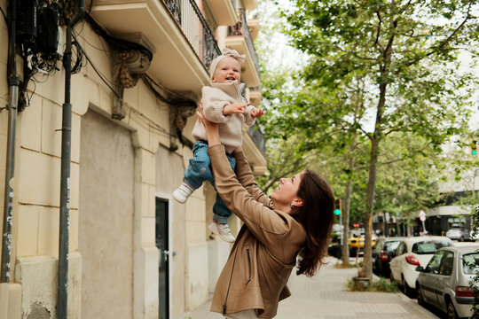 Happy mother holding her laughing baby daughter high in the street 