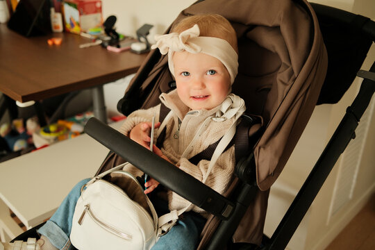 Portrait of little baby girl sitting in the stroller inside the room 