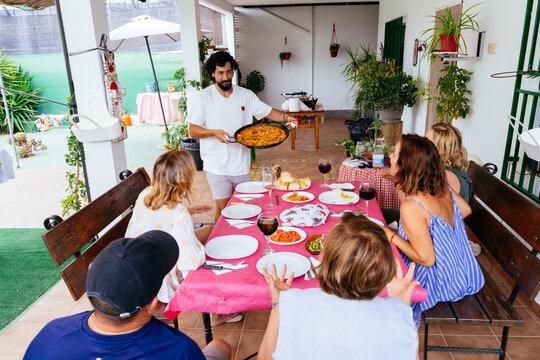 Man serving paella to family and friends outdoors